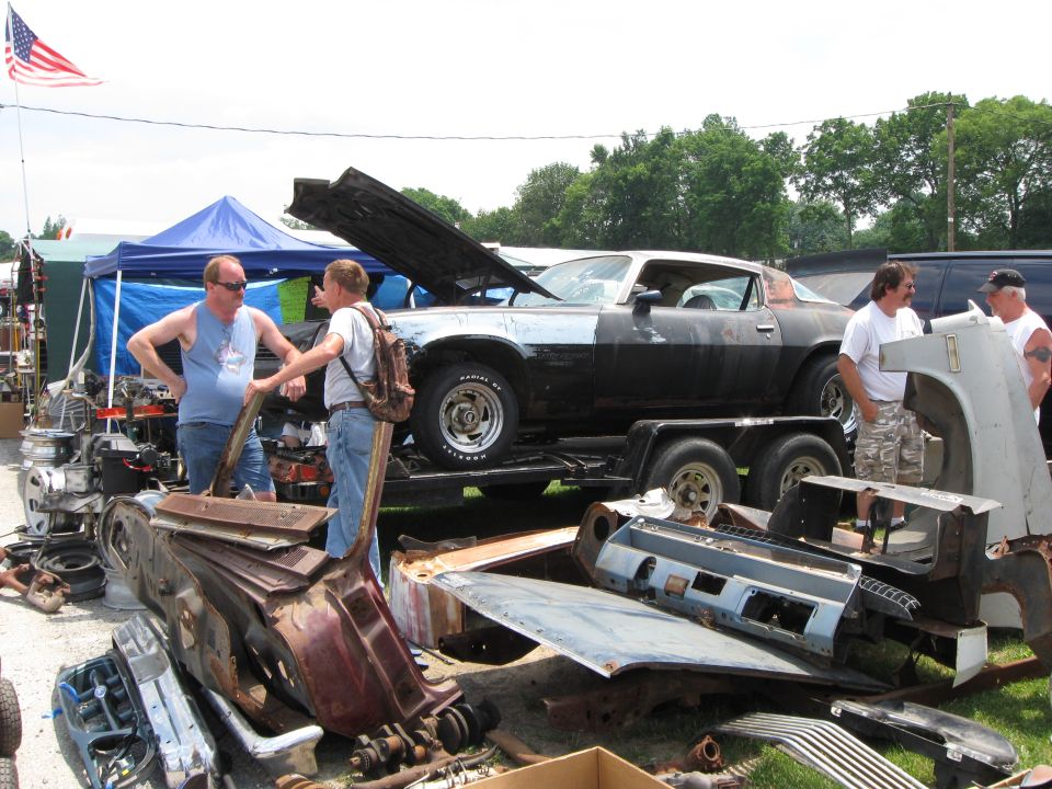 Black and silver muscle car on trailer, hood open, with car parts scattered around