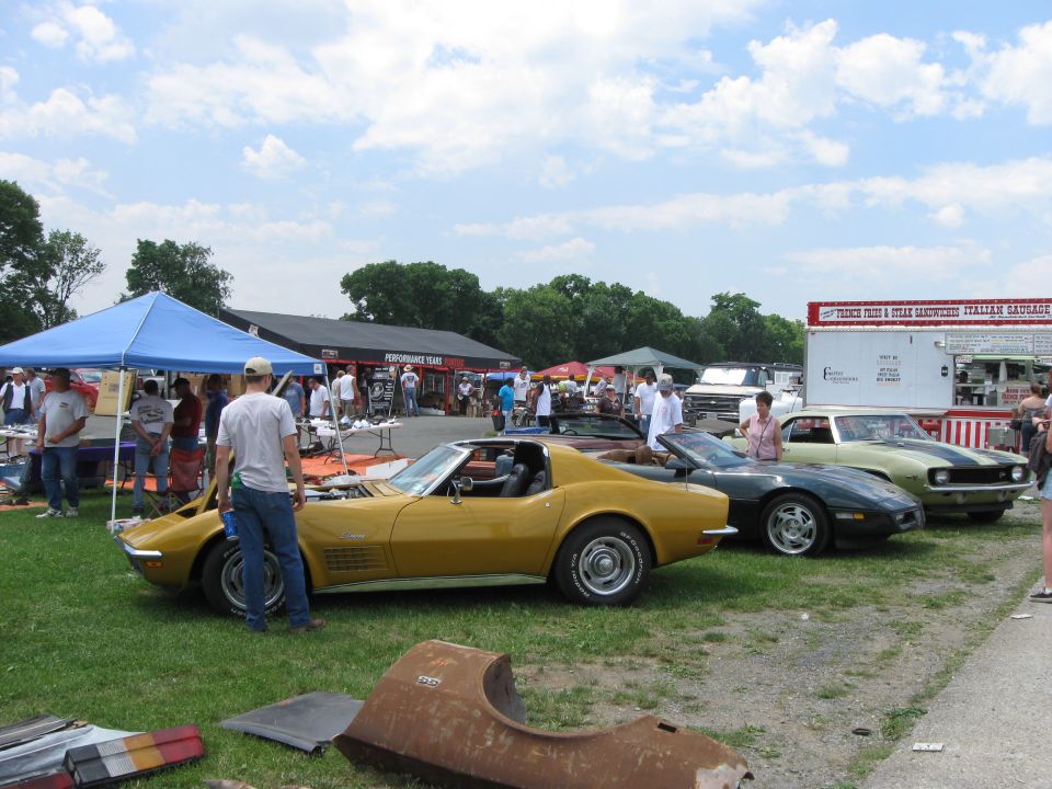 Yellow and dark green classic sports cars parked on grass with people around and a food truck in the background