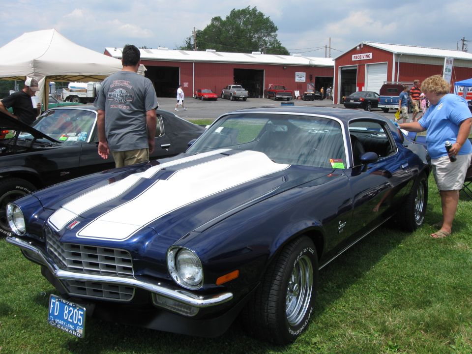 Dark blue Chevrolet Camaro with white racing stripes, front quarter view, parked on grass