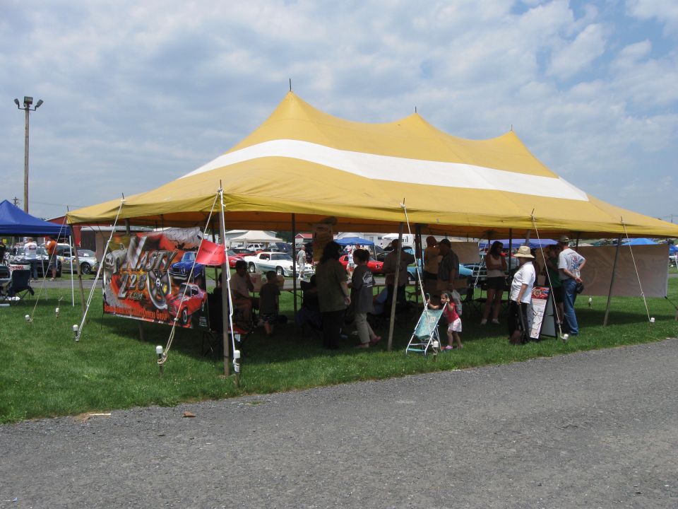 Yellow and white tent with people gathered underneath, cars visible in the background