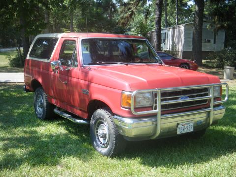 1989 Ford Bronco - This red Ford Bronco is parked on a grassy lawn in front of trees and a mobile home.