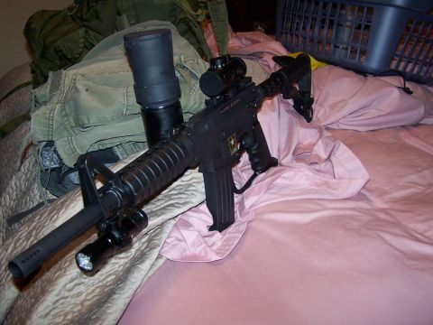 1986 Ford Bronco - An assault rifle with tactical accessories is placed on a bed.