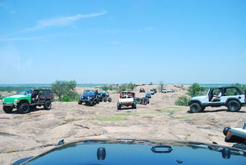 2008 Jeep Wrangler - A convoy of off-road vehicles navigates a rocky, outdoor trail under a clear blue sky.