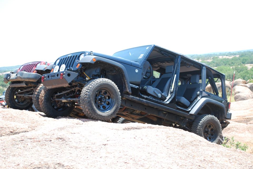 Dark blue 2007 Jeep Wrangler with doors removed, on rocky terrain next to a red Jeep