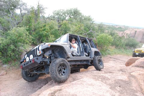 2008 Jeep Wrangler - Two Jeeps navigating a rocky off-road trail with sparse vegetation and large boulders.