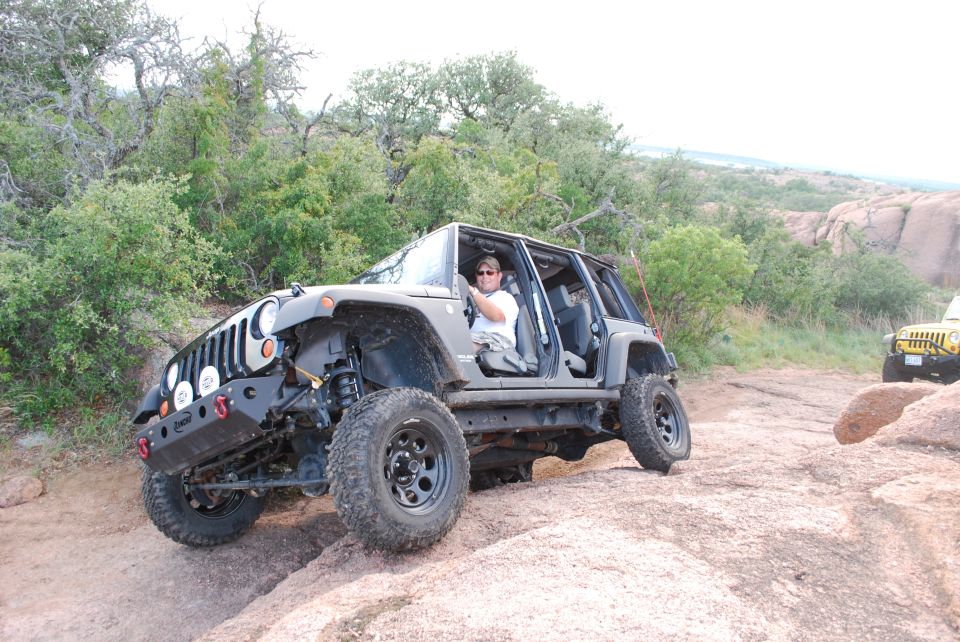 Gray Jeep Wrangler with doors removed driving on rocky terrain, another yellow Jeep visible in background