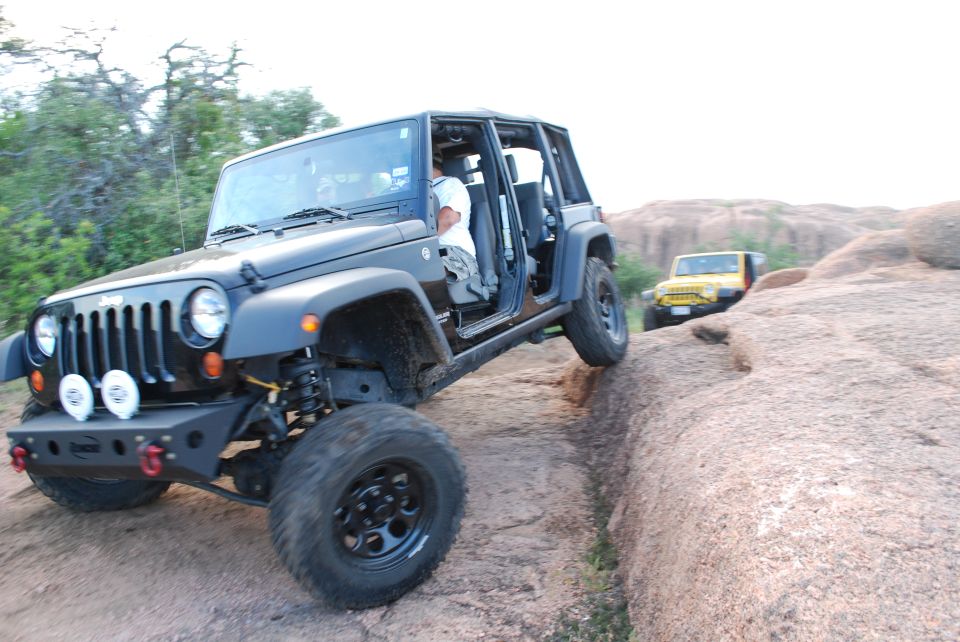 Dark gray Jeep Wrangler climbing over rocks, yellow Jeep in background