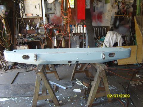 1989 Ford Bronco - A light blue painted rear bumper is displayed on sawhorses in a cluttered workshop.