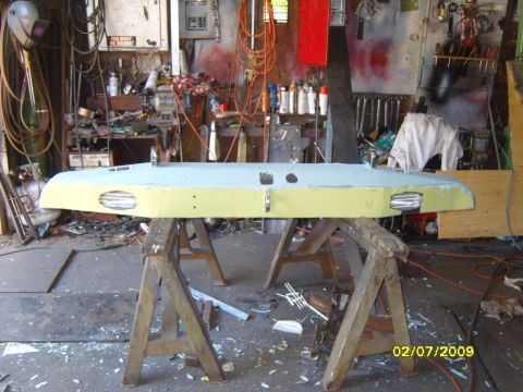 1989 Ford Bronco - Front bumper assembly, painted light blue and yellow, is mounted on sawhorses in a workshop.