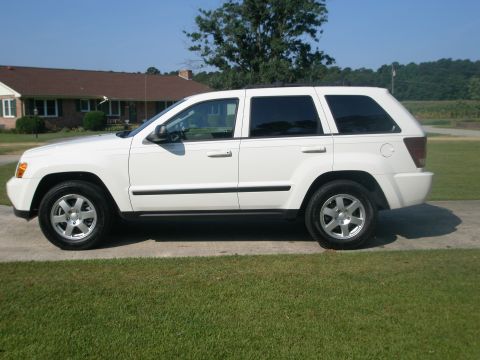 2009 Jeep Grand Cherokee - A white Jeep Grand Cherokee is parked on a paved surface in front of a house.