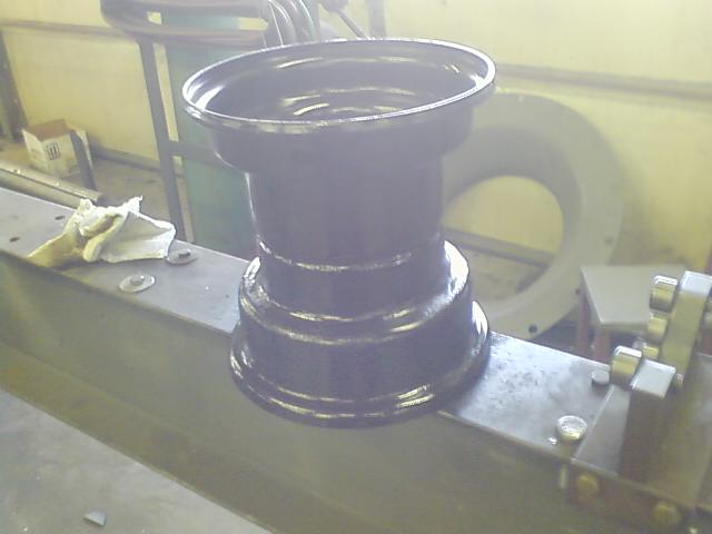 Black steel wheel rim on a metal workbench, with a rag and a large circular object in the background