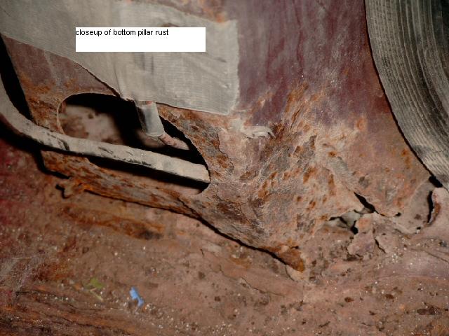 Closeup of heavy rust holes at bottom pillar and rocker panel of a dark red vehicle, tire at right