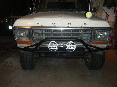 1979 Ford Bronco - A white 1978 Ford Bronco is parked indoors, showing its front grille and bumper with auxiliary lights.
