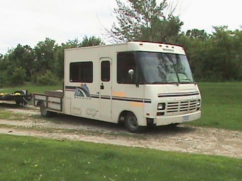 1987 Ford Bronco - This motorhome features a flatbed trailer attached to its rear.