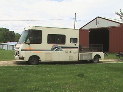 1987 Ford Bronco - This motorhome features a flatbed cargo area behind the cab and is parked near a red barn.