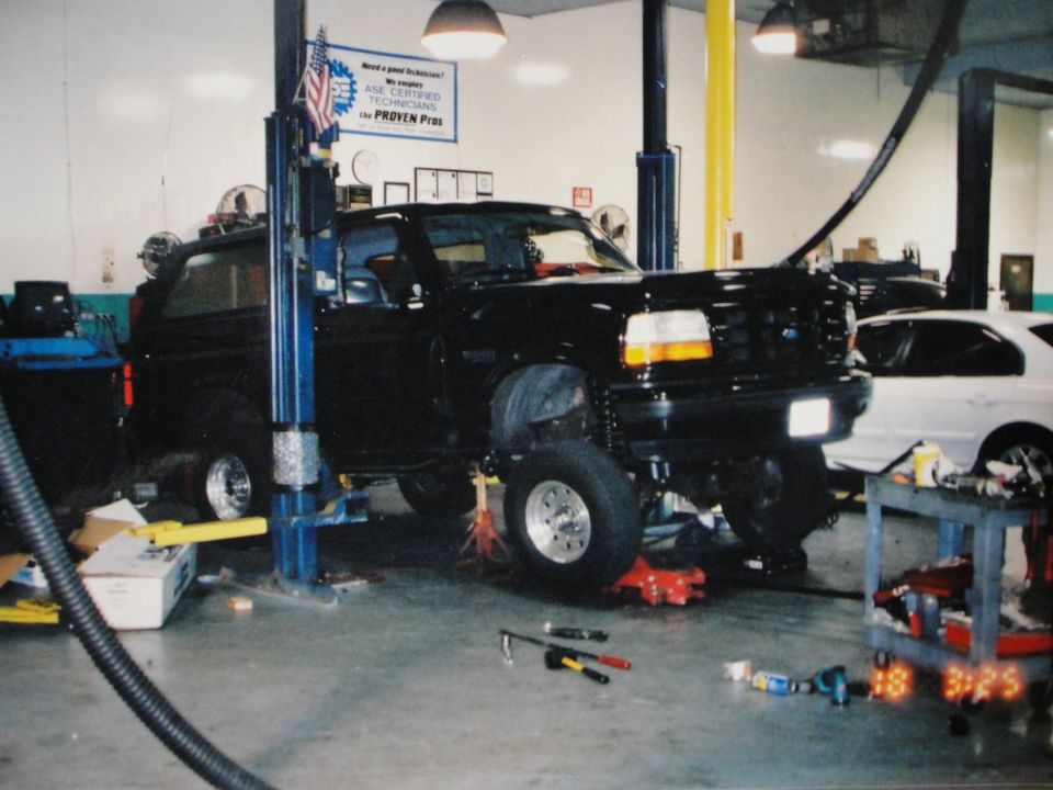 Black SUV on a lift in a garage, with a white car in the background. Tools are on the floor