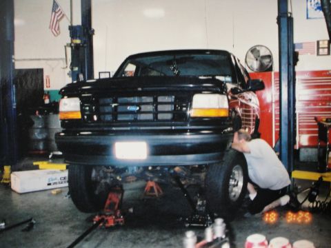 1995 Ford Bronco - Black Ford Bronco in a garage with a mechanic working on the front wheel.