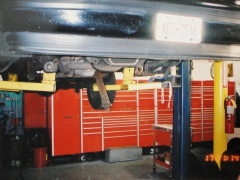 1995 Ford Bronco - Undercarriage view of a dark vehicle, possibly a Ford Bronco, on a lift with a visible license plate.
