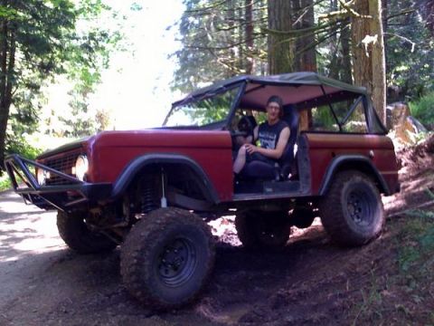 1968 Ford Bronco - A red 1966 Ford Bronco navigates a wooded trail with a driver inside.
