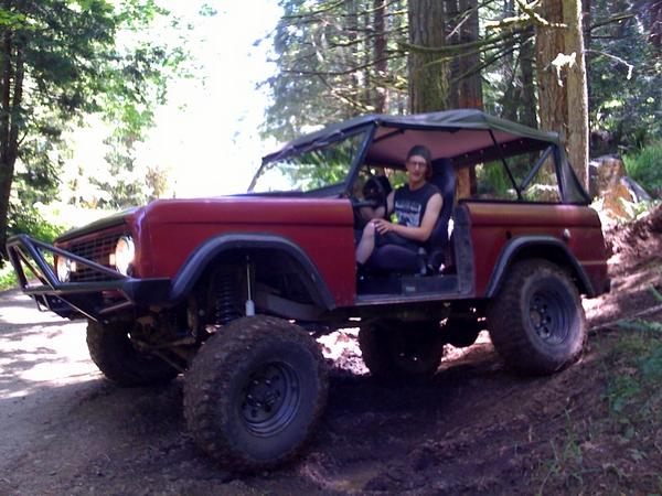 Red 1966 Ford Bronco with off-road modifications driving on a dirt trail