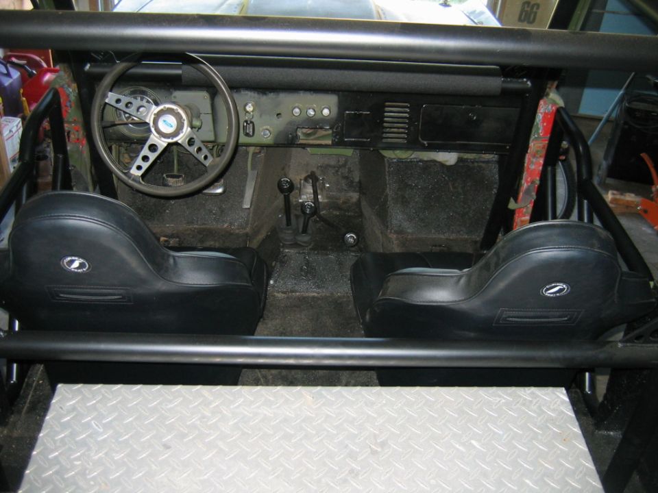 Interior of a vintage Ford Bronco with black bucket seats, a roll cage, and a dashboard with gauges