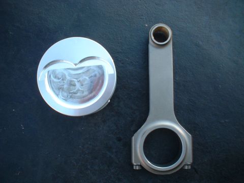 1968 Ford Galaxie - A performance piston with a distinctive heart-shaped valve relief sits next to a connecting rod, likely for an engine build.