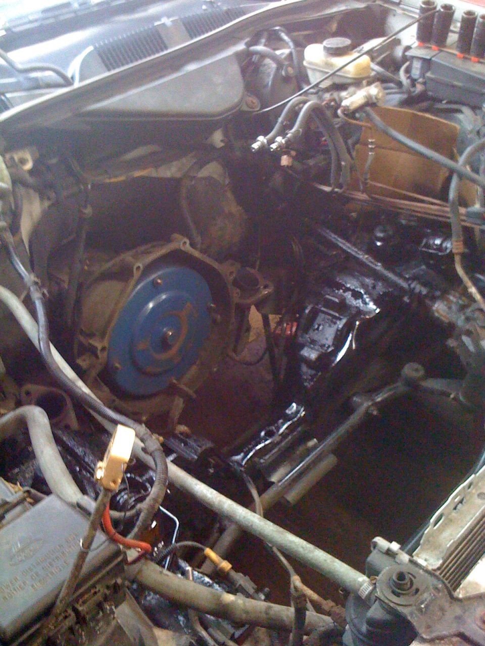 Engine bay showing transmission bell housing and torque converter, with various hoses and wiring