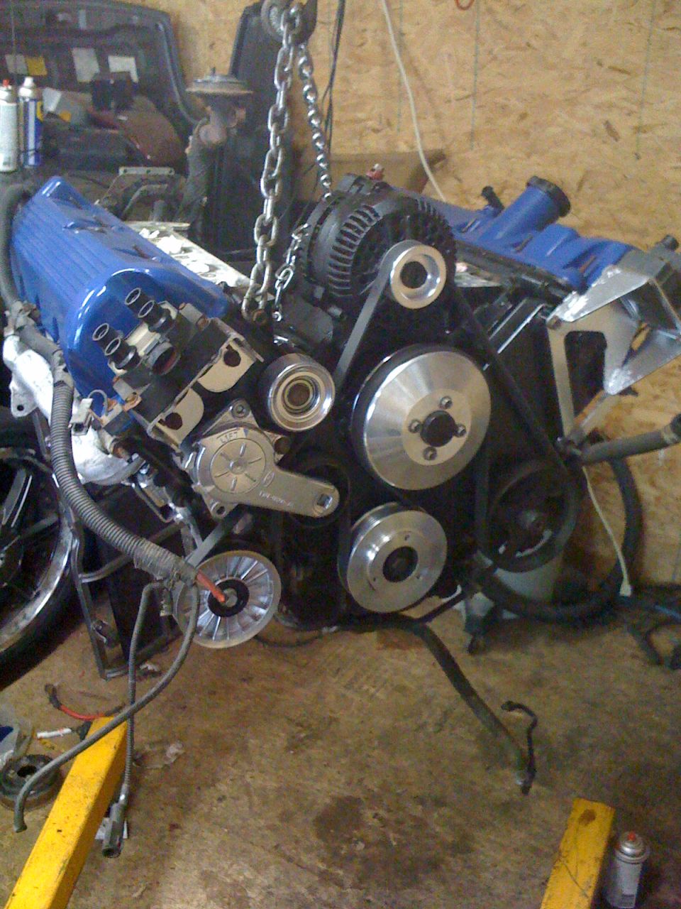 Engine assembly with blue valve covers and chrome pulleys being lifted by a chain