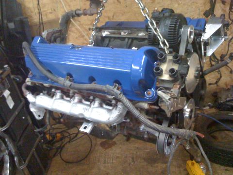 1996 Ford Crown Victoria - Engine assembly, painted blue with silver exhaust manifolds, is shown suspended by chains.