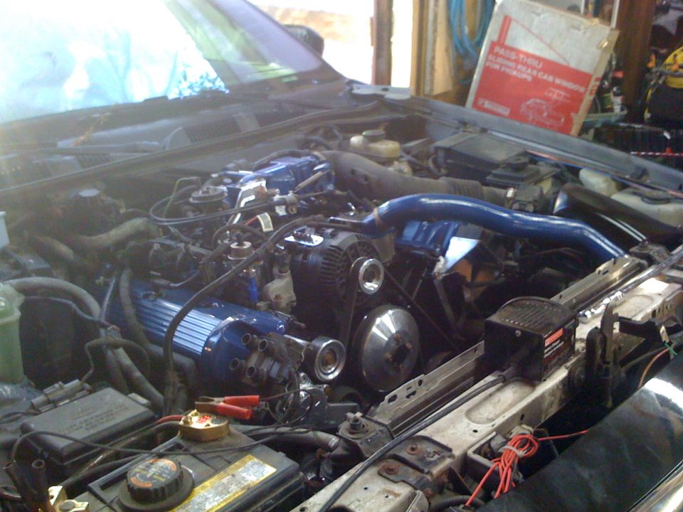 Engine bay with blue painted intake manifold and valve covers, showing alternator and battery