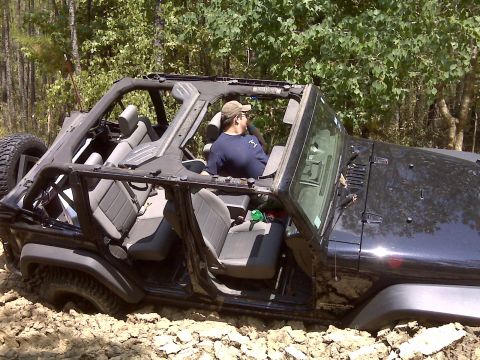 2008 Jeep Wrangler - A black 2008 Jeep Wrangler is stuck in the mud, with its doors and roof removed, as a person sits in the driver's seat.