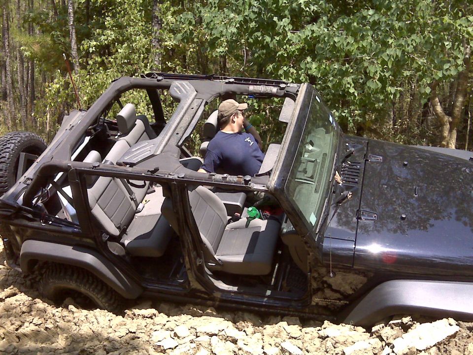 Black 2008 Jeep Wrangler stuck in mud, driver looking back