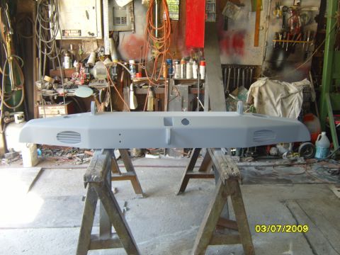1989 Ford Bronco - A gray bumper, likely for a truck or SUV, sits on sawhorses in a cluttered workshop, ready for further work.