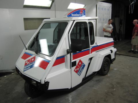 2001 Ford Crown Victoria - A Domino's Pizza branded three-wheeled vehicle is parked indoors with two men standing in the background.