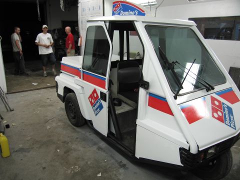 2001 Ford Crown Victoria - A Domino's Pizza branded three-wheeled delivery vehicle is parked indoors with its driver's door open.