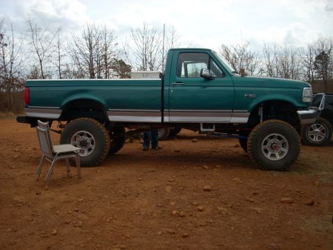 1996 Ford Bronco - This lifted green Ford F-150 pickup truck is seen from the side, with another vehicle partially visible in the background.