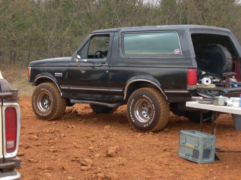 1996 Ford Bronco - A black 1996 Ford Bronco is parked on a dirt lot, its tailgate open revealing camping gear.