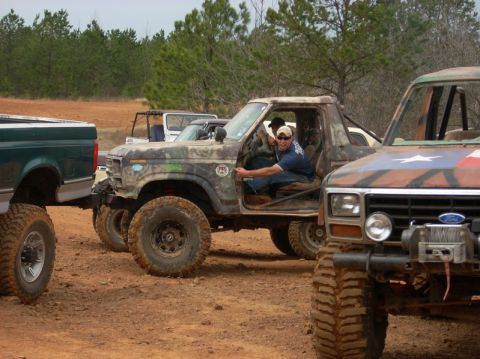 1996 Ford Bronco - A camouflaged off-road SUV is seen from a 3/4 front view, with a man in the driver's seat and other vehicles nearby.