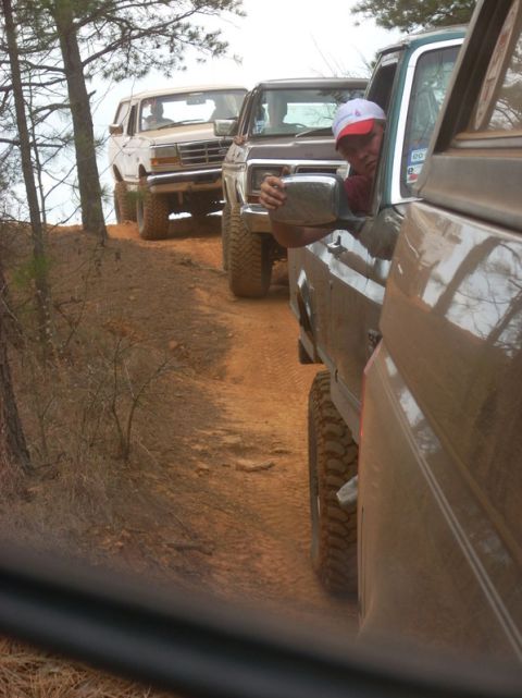 1996 Ford Bronco - A line of off-road vehicles navigates a dusty trail through a wooded area.