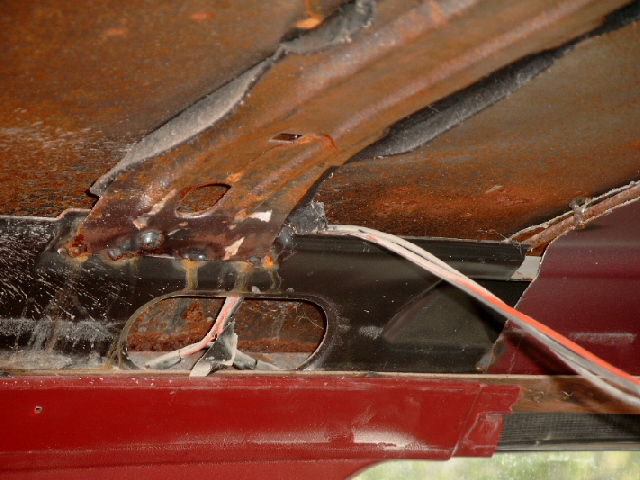 Rusted metal panel with wires visible inside a red vehicle