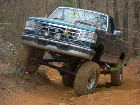 1996 Ford Bronco - A lifted Ford F-Series truck navigates an off-road trail with its front tires angled upwards.