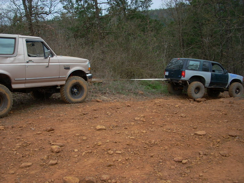 Tan 1992 Ford Bronco towing a dark green and grey SUV on a dirt road