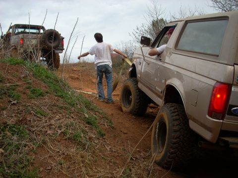 1996 Ford Bronco - Two trucks are navigating a steep, muddy incline during an off-road excursion.