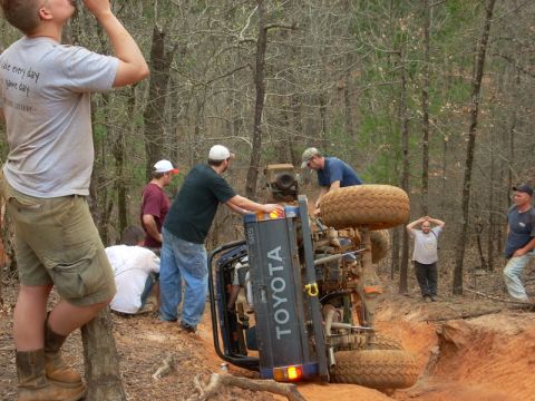 1996 Ford Bronco - People look on as a Toyota truck lies on its side in a wooded area.