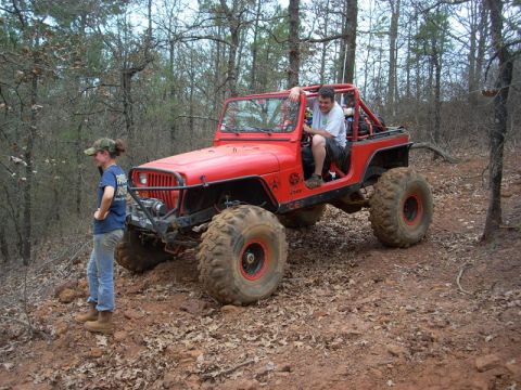 1996 Ford Bronco - Two people are with a red Jeep on a wooded trail.