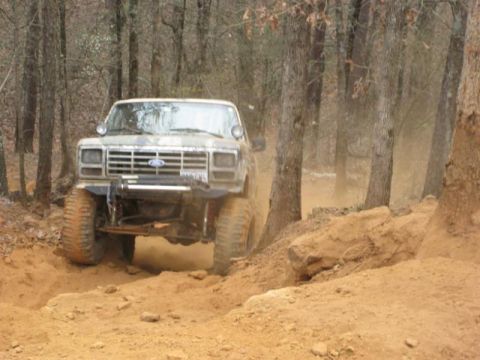 1996 Ford Bronco - A Ford Bronco navigates a challenging off-road trail, kicking up dust among the trees.