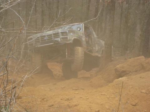 1996 Ford Bronco - Custom off-road truck navigating a challenging dirt trail in a wooded area.