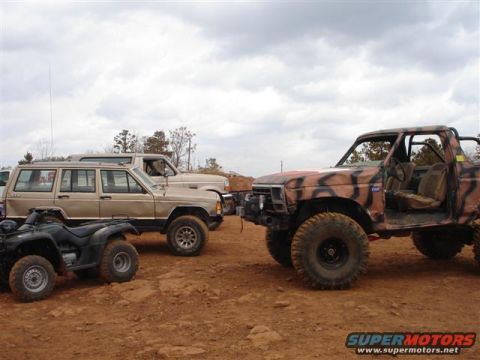 1996 Ford Bronco - Several off-road vehicles, including a camouflaged truck and a tan SUV, are parked on a dirt lot under a cloudy sky.