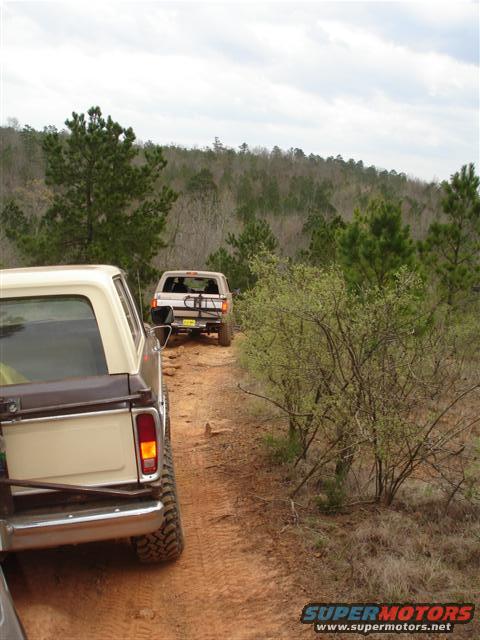 1996 Ford Bronco - Two SUVs navigate a dusty trail surrounded by trees under a cloudy sky.