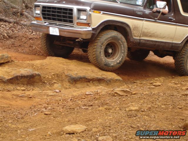 Brown and tan Ford Bronco navigating rocky terrain, front grille and tires visible